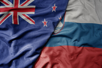 big waving national colorful flag of slovenia and national flag of new zealand .