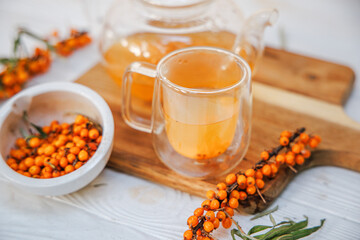 Cup with fragrant vitamin tea from sea buckthorn on a wooden table. Fresh sea buckthorn berries on a branch are ready for the preparation of a healing drink