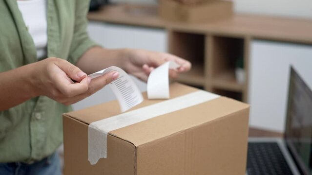 Hands of female consumer stick barcode on cardboard box with yellow sticker with word Return sitting at workplace with statement concept of returning parcel