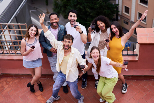 Multiracial group of friends gathering together outdoors in a terrace looking up to the camera lively.
