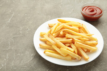 French fries on plate with ketchup in bowl on grey background.