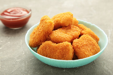 Chicken nuggets with ketchup on plate on grey background.