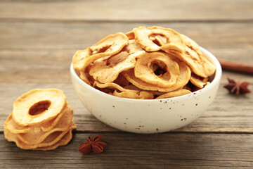 Dried apple chips in a bowl with fresh apple on grey wooden background.