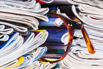 Stack of newspapers and magazines and reading glasses