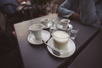 friends hands holding cups of milk and coffee on wooden table in the street of Italy. Female hands hold a coffee cup. Coffee break. 