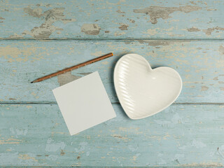 Heart shaped plate, paper, pencil on vintage wooden background. Top view. - 728760735