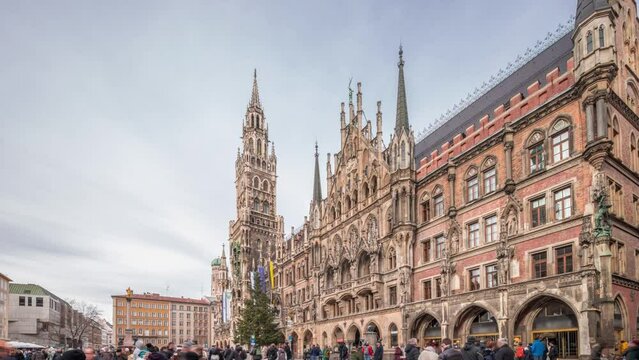 Main facade of the New Town Hall (Neues Rathaus) building at the northern part of Marienplatz timelapse hyperlapse in Munich. Fischbrunnen fountain in front. Cloudy sky. Bavaria, Germany.