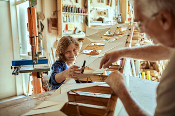 Grandfather and grandson building a wooden model in a workshop
