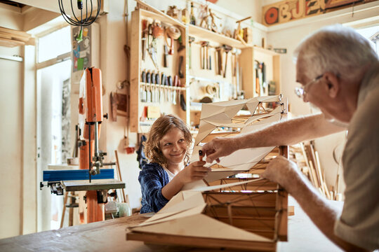 Grandfather and grandson building a wooden model in a workshop