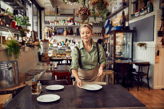 Middle aged waitress setting up plates on restaurant table