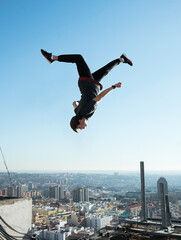young boy doing parkour a backflip over blue sky on rooftop