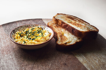 Scrambled eggs in a bowl served on a wooden plate with toasts; isolated on white background with copyspace