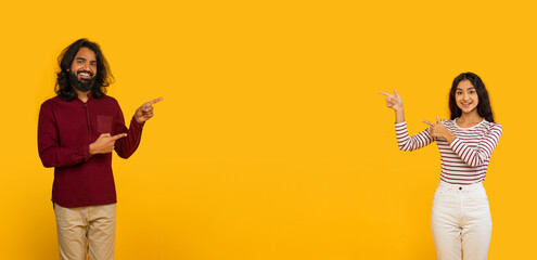 Obraz premium Positive young indian man and woman pointing at blank space