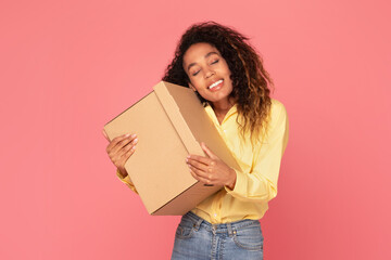 Joyful young black woman hugging parcel, smiling on pink backdrop
