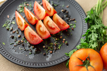 Tomatoes with parsley, chives, black pepper, himalayan salt and olive oil on a black plate.