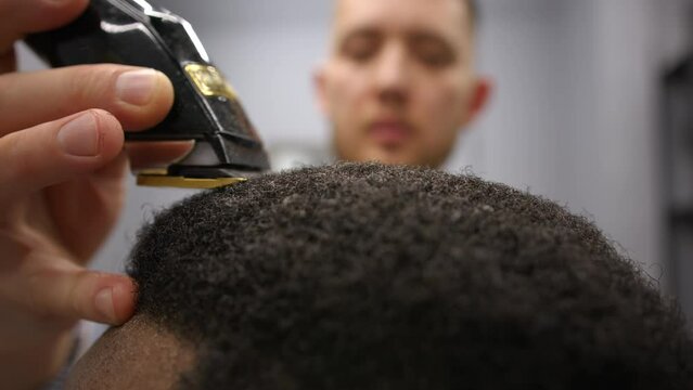 Hairdresser cuts African American man with professional hair clipper in salon