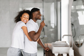 Black Woman Hugging Husband While Man Brushing Teeth In Bathroom