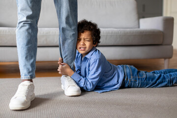 Upset child boy clinging to father's leg at home