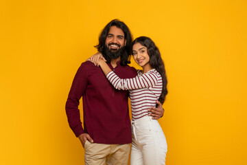 Happy young indian man and woman embracing on yellow background