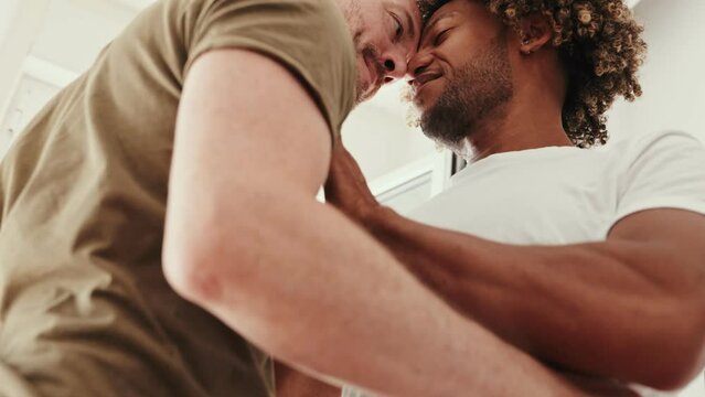 Intimate moment between a diverse same-sex couple as they dance and kiss, portraying love and connection in a cozy home setting.