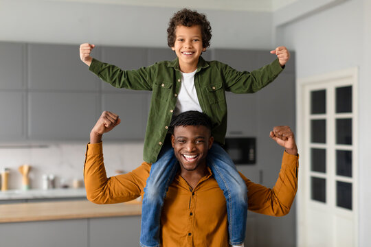 Joyful black father and son flexing muscles together at home