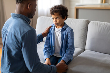 Black father comforting upset preteen son at home