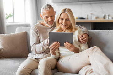 Positive retired couple using digital tablet at home