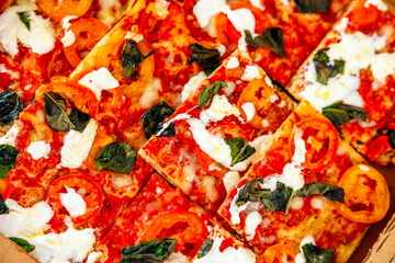 Freshly baked pizza with tomato, mozzarella and basil cutting into a slices