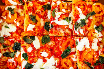 Top view of an Italian freshly backed pizza with tomato, mozzarella and basil cutting into slices