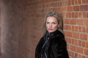 Portrait of a beautiful blonde woman posing against a brick wall, looking at the camera