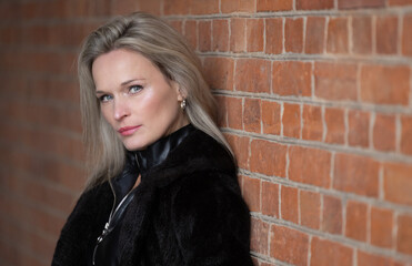 Portrait of a beautiful blonde woman posing against a brick wall, looking at the camera