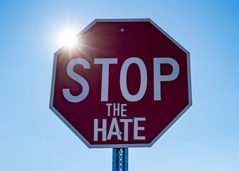 Red stop sign with sunshine blue sky background reading stop the hate