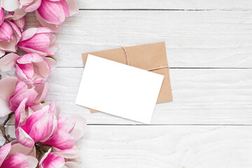 Blank greeting card with spring pink magnolia flowers on white wooden background. Mock up. Flat lay. Top view. Womens day, Mothers day, Wedding or anniversary invitation