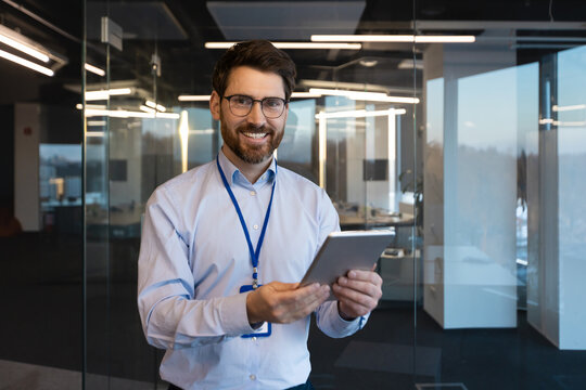 Portrait of mature experienced programmer system administrator, man smiling and looking at camera with tablet computer in hands, mature worker testing new software inside office at workplace.
