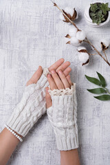 Cropped shot of woman's hands in white short mittens with lace. Hands are on a light surface, flowers are located nearby.