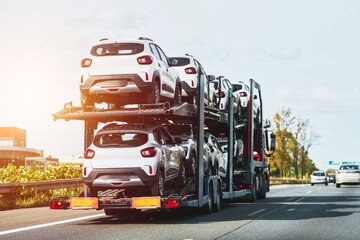 Car dealership delivery. New cars on a hydraulic trailer are ready for delivery and sale. A car transporter truck carries many cars on a two-level modular ramp. - obrazy, fototapety, plakaty