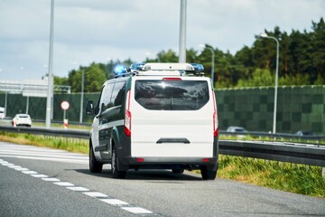 A police van with a mobile radar camera monitors the speed of traffic on a highway. A warning sign of speed limit and fine is placed on the road. A concept of road safety and enforcement.