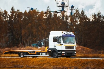 A Car Carrier Tow Truck Driving Fast on the Road with No Vehicle Loaded. A Modern and New Tow Truck Transporter with Space for Text on the Highway in Summer Landscape