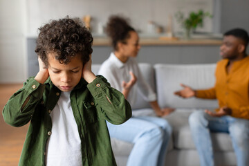 Child boy covers ears while parents argue in the background