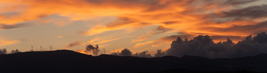 Panorama shot of clean energy power concept with wind turbine on top of a mountain during dramatic sunset in zakynthos, Greece