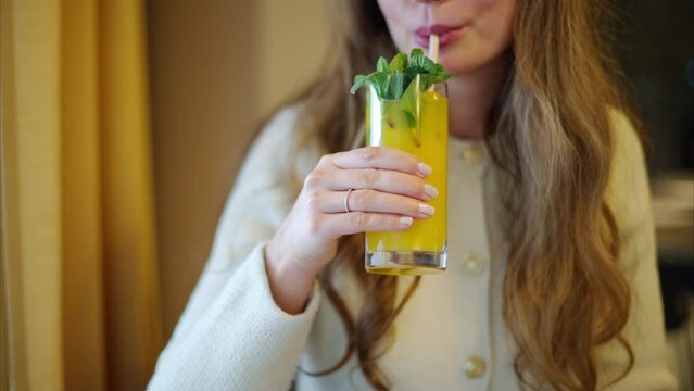 Woman drinking fresh orange lemonade with mint leaves and paper straw