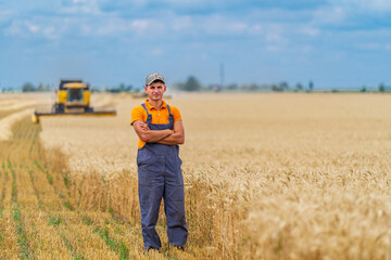 Farmer stands in wheat field with combine harvester in the background