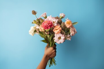 African female's hands gracefully holding an assorted bouquet of roses and other flowers against a striking blue background