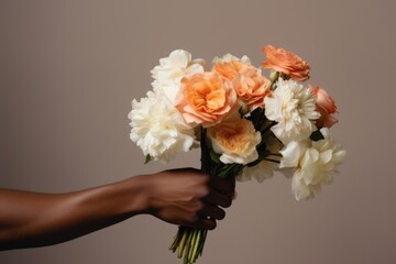 closeup of a strong hand with dark skin tone, delicately holding a bouquet of soft white and peach roses
