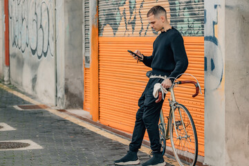 fashionable young man with mobile phone and bicycle in urban background
