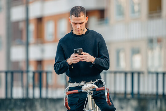 urban young man with mobile phone on top of the bicycle in the street
