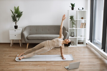 Mature woman in tight sports clothes taking up Side Plank Pose on living room floor with rubber mats during yoga practice. Active slim lady building overall flexibility using Vasisthasana exercise.