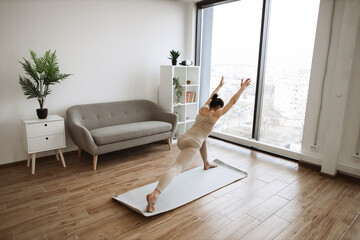Mature brunette practising Warrior I Halfway Fold during yoga exercise at home. Caucasian woman...