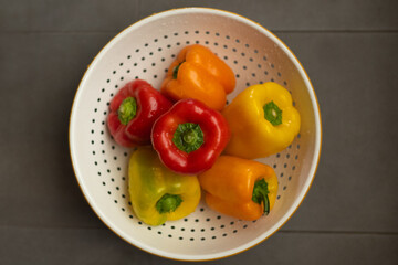 A group of bright, colorful bell peppers inside a colander from above.