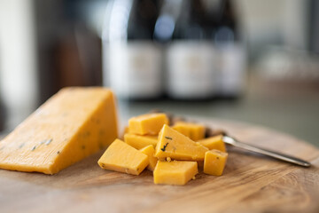 Cheddar cheese cut on an olive wooden board with a wine bottle in the background.